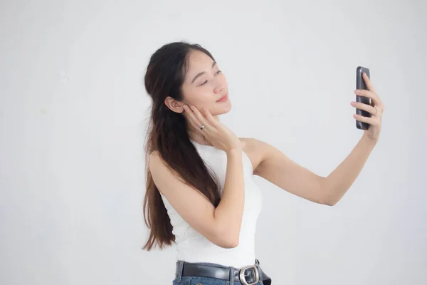 タイの肖像中国大人美しいです女の子ホワイトシャツブルージーンズ使用して彼女のスマートフォンSelfie — ストック写真