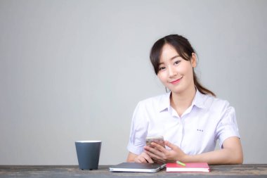 Taylandlı liseli üniformasının portresi. Güzel bir kız. Telefonunu kullanıp gülümsüyor.