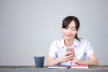 Taylandlı liseli üniformasının portresi. Güzel bir kız. Telefonunu kullanıp gülümsüyor.