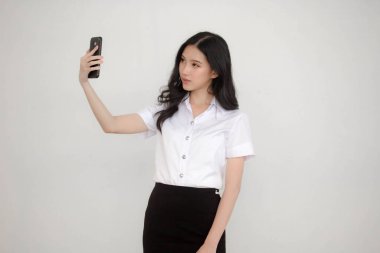 Taylandlı yetişkin öğrenci üniformasının portresi. Güzel kız akıllı telefonuyla selfie çekiyor.
