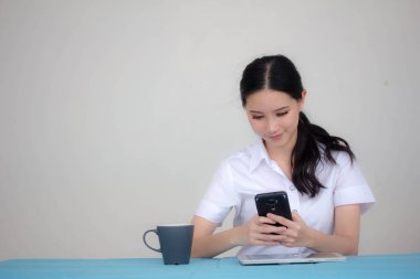Taylandlı yetişkin öğrenci üniformasının portresi. Akıllı telefonunu kullanan güzel bir kız.