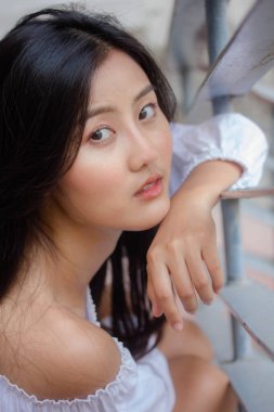 Taylandlı yetişkin güzel kız portresi. Beyaz gömlek, mavi kot pantolon, rahatla ve gülümse.