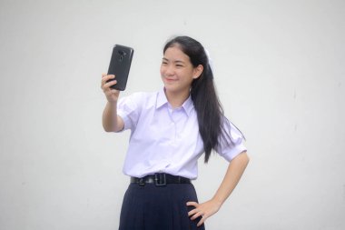 Taylandlı liseli üniformasının portresi. Güzel kız akıllı telefonuyla selfie çekiyor.