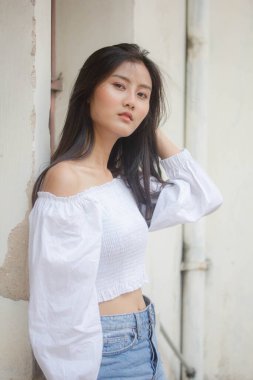 Taylandlı yetişkin güzel kız portresi. Beyaz gömlek, mavi kot pantolon, rahatla ve gülümse.