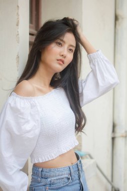 Taylandlı yetişkin güzel kız portresi. Beyaz gömlek, mavi kot pantolon, rahatla ve gülümse.