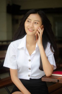 Taylandlı yetişkin öğrenci üniformasının portresi. Güzel bir kız akıllı telefondan arıyor.