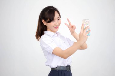 Taylandlı liseli üniformasının portresi. Güzel kız akıllı telefonuyla selfie çekiyor.