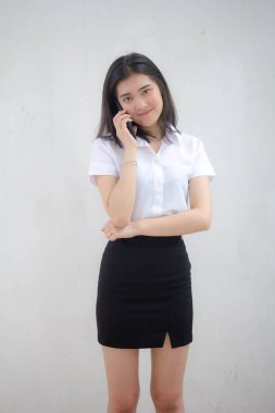 Taylandlı yetişkin öğrenci üniformasının portresi. Güzel bir kız akıllı telefondan arıyor.