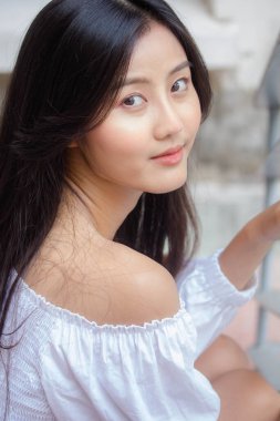 Taylandlı yetişkin güzel kız portresi. Beyaz gömlek, mavi kot pantolon, rahatla ve gülümse.