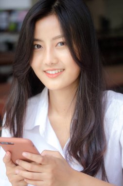 Taylandlı yetişkin öğrenci üniformasının portresi. Akıllı telefonunu kullanan güzel bir kız.