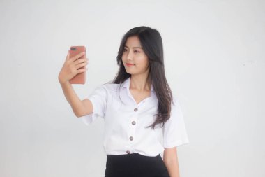 Taylandlı yetişkin öğrenci üniformasının portresi. Güzel kız akıllı telefonuyla selfie çekiyor.