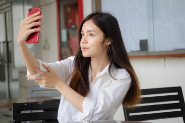 Taylandlı yetişkin kadınların portresi beyaz gömlekli akıllı telefon özçekimini kullanıyor.