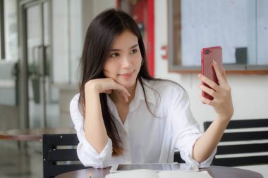 Taylandlı yetişkin kadınların portresi beyaz gömlekli akıllı telefon özçekimini kullanıyor.