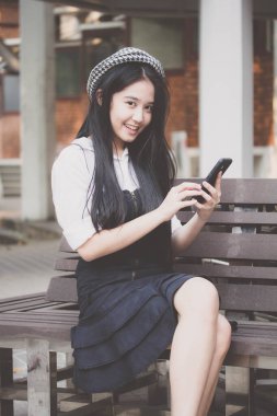 Taylandlı genç bir kızın portresi. Telefonunu kullanıp gülümsüyor.