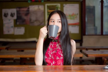 Taylandlı genç bir kızın portresi Çin elbisesi giymiş sıcak fincan içiyor.