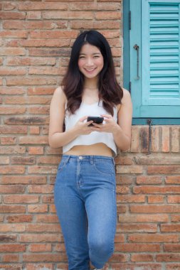Tayland portresi. Yetişkin, güzel bir kız. Akıllı telefonunu kullanan beyaz gömlek, mavi kot pantolon.