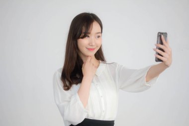 Taylandlı yetişkin kadınların portresi beyaz gömlekli akıllı telefon özçekimini kullanıyor.