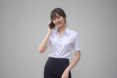 Taylandlı yetişkin öğrenci üniformasının portresi. Güzel bir kız akıllı telefondan arıyor.