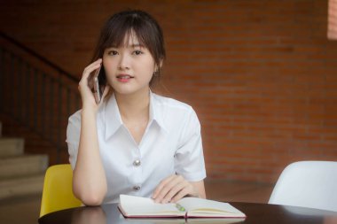 Taylandlı yetişkin öğrenci üniformasının portresi. Güzel bir kız akıllı telefondan arıyor.