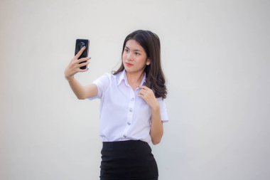 Yetişkin öğrenci üniforması güzel kız akıllı telefonuyla selfie çekiyor.