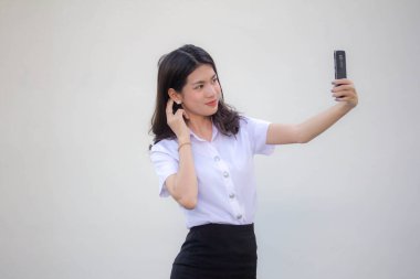 Yetişkin öğrenci üniforması güzel kız akıllı telefonuyla selfie çekiyor.