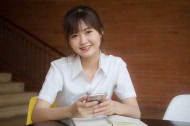 Taylandlı yetişkin öğrenci üniformasının portresi. Akıllı telefonunu kullanan güzel bir kız.