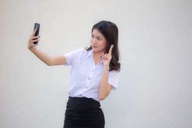 Yetişkin öğrenci üniforması güzel kız akıllı telefonuyla selfie çekiyor.