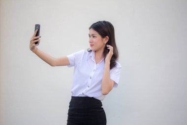 Yetişkin öğrenci üniforması güzel kız akıllı telefonuyla selfie çekiyor.