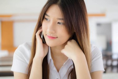 Taylandlı yetişkin öğrenci üniformasının portresi. Güzel bir kız akıllı telefondan arıyor.