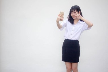 Yetişkin öğrenci üniforması güzel kız akıllı telefonuyla selfie çekiyor.