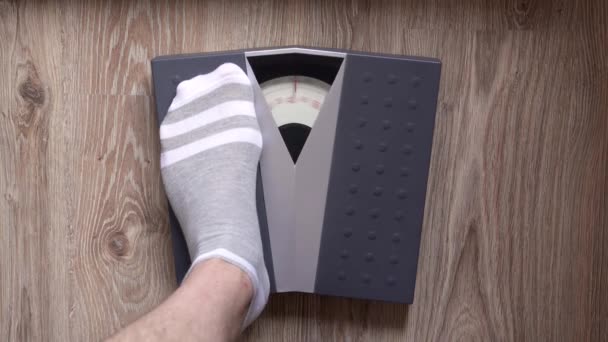 男は体重をチェックするために機械的な床のスケールに足を踏み入れる 太りすぎや肥満に取り組むという概念 — ストック動画