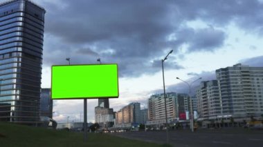 Konsepti uydur. Şehir yolunda akşam gökyüzünün arka planına karşı yeşil ekran reklam panosu.