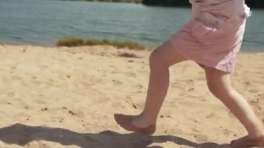 Yakın plan oyuncu, beyaz bir kız kumsalın beyaz kumlarında koşuyor. Kumlu sahil boyunca koşan çocuk ayakları.
