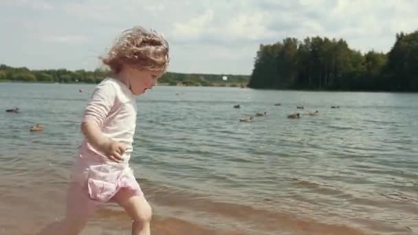 분홍색 치마를 소녀가 해변에서 다닌다 바람에 나부끼는 곱슬머리의 소녀는 해변의 — 비디오