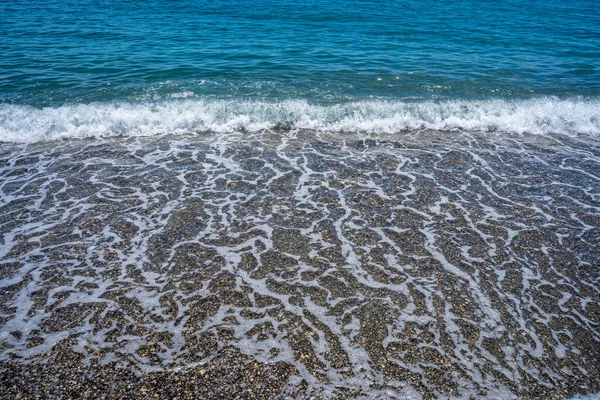 泡沫波带着卵石到达平静的海滩的前景 — 图库照片