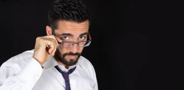 Resmi kıyafetlerle gözlüklerin üzerinden bakan yakışıklı genç sakallı portresi. Kopya alanı olan optik erkek model. Kravatlı ve gömlekli çekici stil sahibi bir iş adamı. Siyah arkaplan.