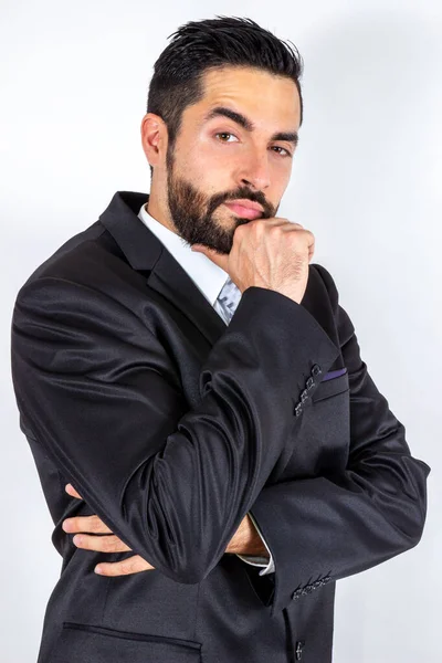 Takım elbiseli yakışıklı küstah işadamı, kaşlarını kaldırıyor, kollarını kavuşturup tatmin olduğunu düşünüyor. Çekici, genç, şık, sakallı adam sorgulanıyor. Orta boy. Beyaz arkaplan.