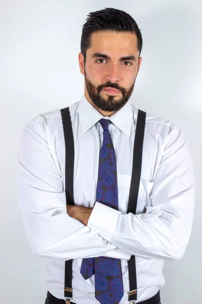 Çapraz kollu, resmi giysili yakışıklı, sakallı adam. Gömlek, pantolon askısı ve kravatlı çekici bir iş adamı. Orta boy. Beyaz arkaplan.