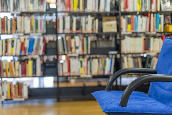 Public library interior with unoccupied blue armchair and lots of books on the shelves