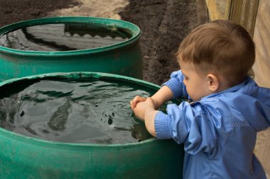 Bir çocuk çiftlikteki su varilinde yüzünü yıkıyor.