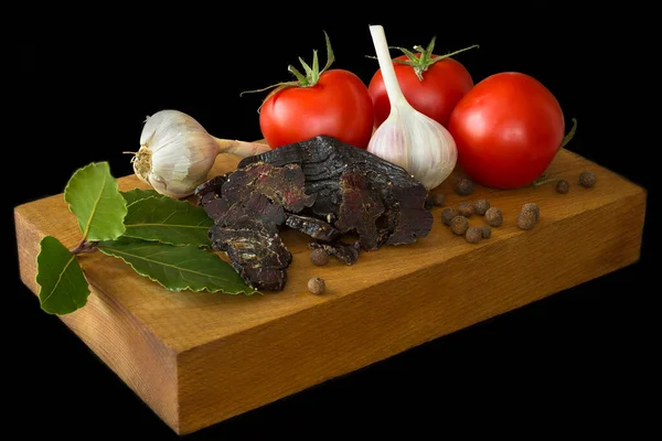 Domates, sarımsak, kurutulmuş geyik eti, ahşap bir tahtada körfez yaprakları. Siyah arka plan. izole et.