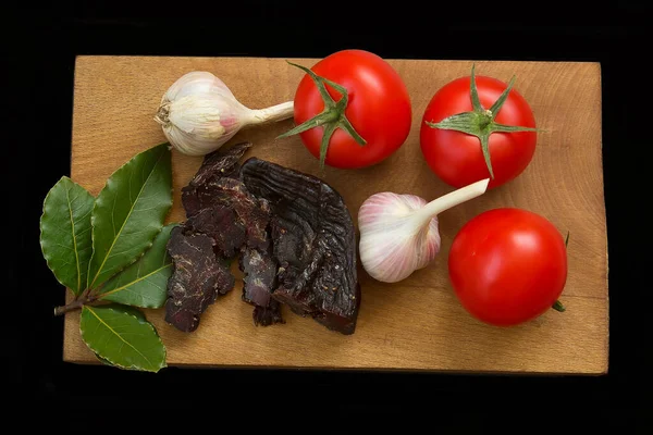Domates, sarımsak, kurutulmuş geyik eti, ahşap bir tahtada körfez yaprakları. Siyah arka plan. İzole et. tepeden görünüm.