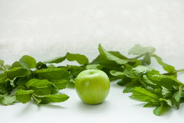 Beyaz arkaplanda nane yaprağı ve kopyalama alanı olan yeşil elma.