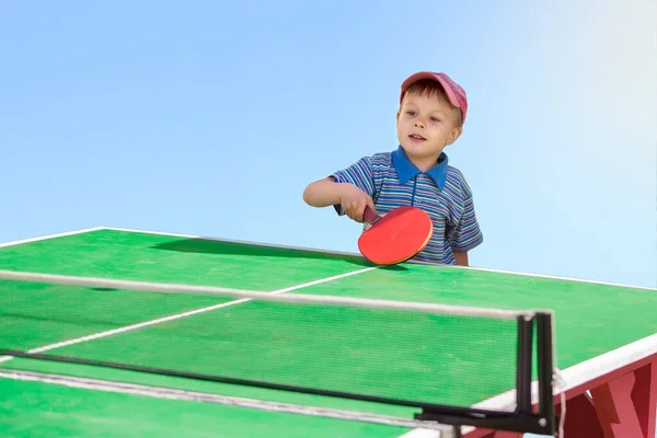 Çocuk açık havada masa tenisi oynuyor..