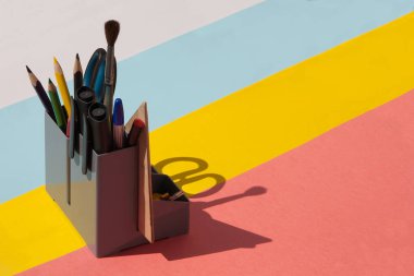 Renkli bir arkaplan üzerinde kalem, kalem, cetvel, makas ve fırça ile okul düzenleyicisi.