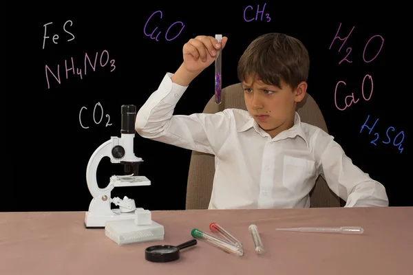 Çocuk elinde bir matarayla karanlık bir arka planda kimya okuyor..