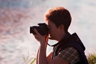Suyun arka planında elinde kamera olan bir kadın fotoğrafçının silueti..