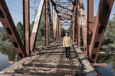 Adam terk edilmiş bir demiryolu köprüsünde duruyor. Nehir boyunca ormandaki demir köprü