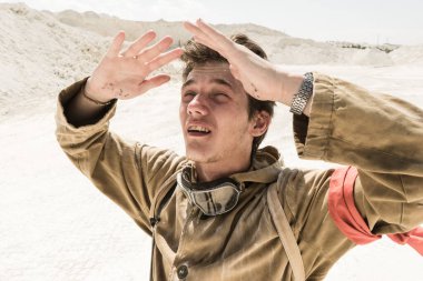 Beyaz kumların arasında bir adamın yüzüne yakın çekim. Yüzünde ter var. Kıyamet sonrası dünyada takipçi bir sapık..