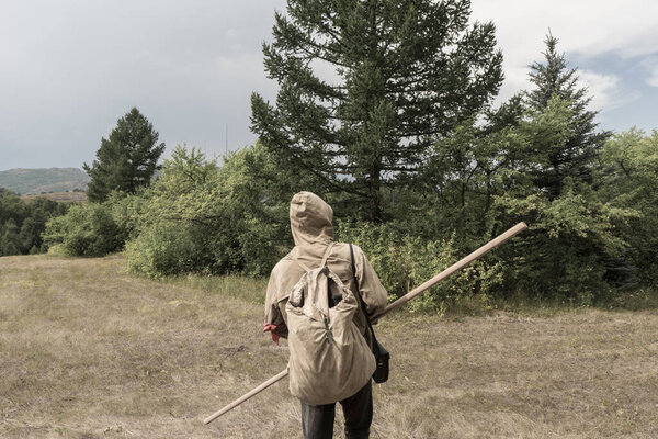 Back view of tourist man with a backpack standing ready to travel on green forest background. Stalker in the post-apocalyptic world.